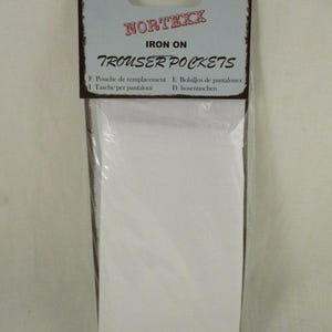 以下が含まれることがあります： 白いアイロン接着のズボンのポケットが1組入ったパッケージ。パッケージには「NORTEXX IRON ON TROUSER POCKETS」と表示され、英語、フランス語、ドイツ語、スペイン語、イタリア語の指示が含まれています。