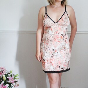 May include: A white slip dress with a floral print and black lace trim. The dress has a V-neckline and thin straps.