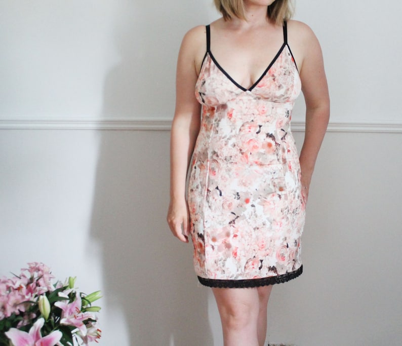 May include: A white slip dress with a floral print and black lace trim. The dress has a V-neckline and thin straps.