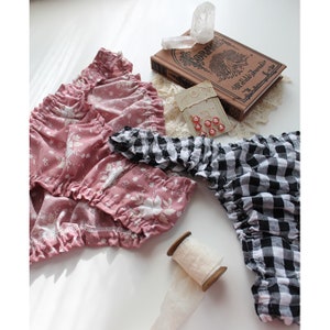 Op de afbeelding: Twee paar geruite stoffen shorts. Een paar is roze met een bloemenprint en het andere is zwart-wit geruit.