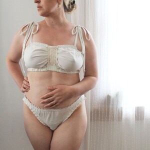 Op de afbeelding: Witte lingerie set met kant, bestaande uit een bandeau top en een geruit onderstuk.