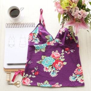 Puede incluir: Top de tirantes de color morado con estampado floral. La parte superior tiene un escote en V y un ajuste holgado.