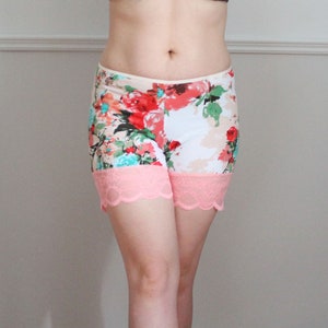 May include: Floral print shorts with a pink lace trim. The shorts are white with pink, red, and blue flowers.