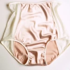 May include: Peach-colored satin underwear with white lace trim. The underwear has a high waist and a full coverage back.