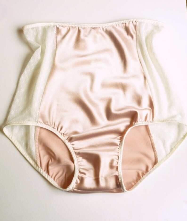 May include: Peach-colored satin underwear with white lace trim. The underwear has a high waist and a full coverage back.