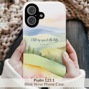 May include: White phone case featuring a watercolor landscape with rolling green hills, blue mountains, and a pink and yellow sky. The text "I lift my eyes to the hills" and "Psalm 121:1" are displayed. The bottom of the case reads "Psalm 121:1 Bible Verse Phone Case."