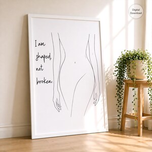 Op de afbeelding: Een witgelijste print met een minimalistische lijntekening van een menselijke figuur. Het kunstwerk bevat de tekst "I am shaped, not broken" in zwart schrift. Een kleine plant in een witte pot staat op een houten kruk.