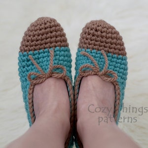 Pode incluir: Um par de pantufas de crochê com a parte superior marrom e a inferior azul turquesa. As pantufas têm um laço marrom na parte da frente.