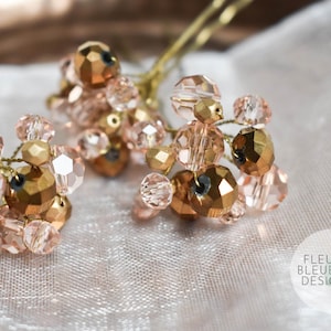May include: Three hair pins with clusters of rose-gold and gold beads. The beads are faceted and arranged on thin, gold wires. The background is a soft, white fabric. The Fleur Bleue Design logo is in the bottom right corner.