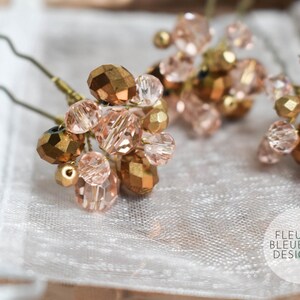 May include: Close-up of several hair pins featuring clusters of faceted, gold and blush-coloured beads. The beads are arranged on thin, wavy, metal pins. The pins rest on a white, textured surface. The Fleur Bleue Design logo is visible.