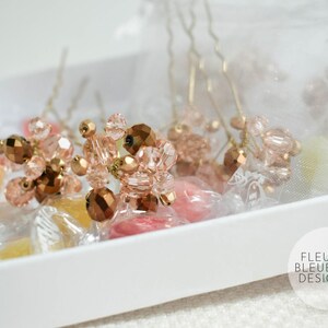 May include: Close-up of hair pins with clusters of faceted beads in shades of rose gold and brown. The pins are arranged in a white tray with wrapped sweets. The Fleur Bleue Design logo is visible in the bottom right corner.