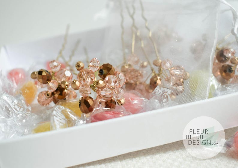 May include: Close-up of hair pins with clusters of faceted beads in shades of rose gold and brown. The pins are arranged in a white tray with wrapped sweets. The Fleur Bleue Design logo is visible in the bottom right corner.