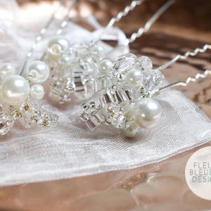 Peut inclure: Trois &eacute;pingles &agrave; cheveux argent&eacute;es orn&eacute;es de grappes de perles blanches artificielles et de perles de cristal transparentes &agrave; facettes. Chaque &eacute;pingle poss&egrave;de une tige m&eacute;tallique ondul&eacute;e. Un logo blanc avec FLEUR BLEUE DESIGN.com est visible.