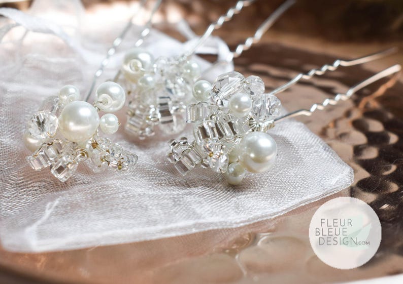 Peut inclure: Trois &eacute;pingles &agrave; cheveux argent&eacute;es orn&eacute;es de grappes de perles blanches artificielles et de perles de cristal transparentes &agrave; facettes. Chaque &eacute;pingle poss&egrave;de une tige m&eacute;tallique ondul&eacute;e. Un logo blanc avec FLEUR BLEUE DESIGN.com est visible.