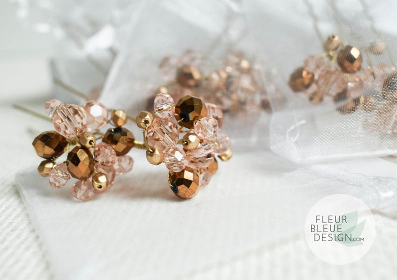 May include: Close-up of several hair pins with clusters of rose gold and bronze beads. The pins are arranged on a white surface with a sheer, white fabric in the background. The Fleur Bleue Design logo is visible.