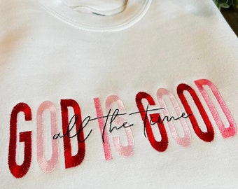 May include: White sweatshirt with the phrase "God is good all the time" embroidered in red, pink, and white.