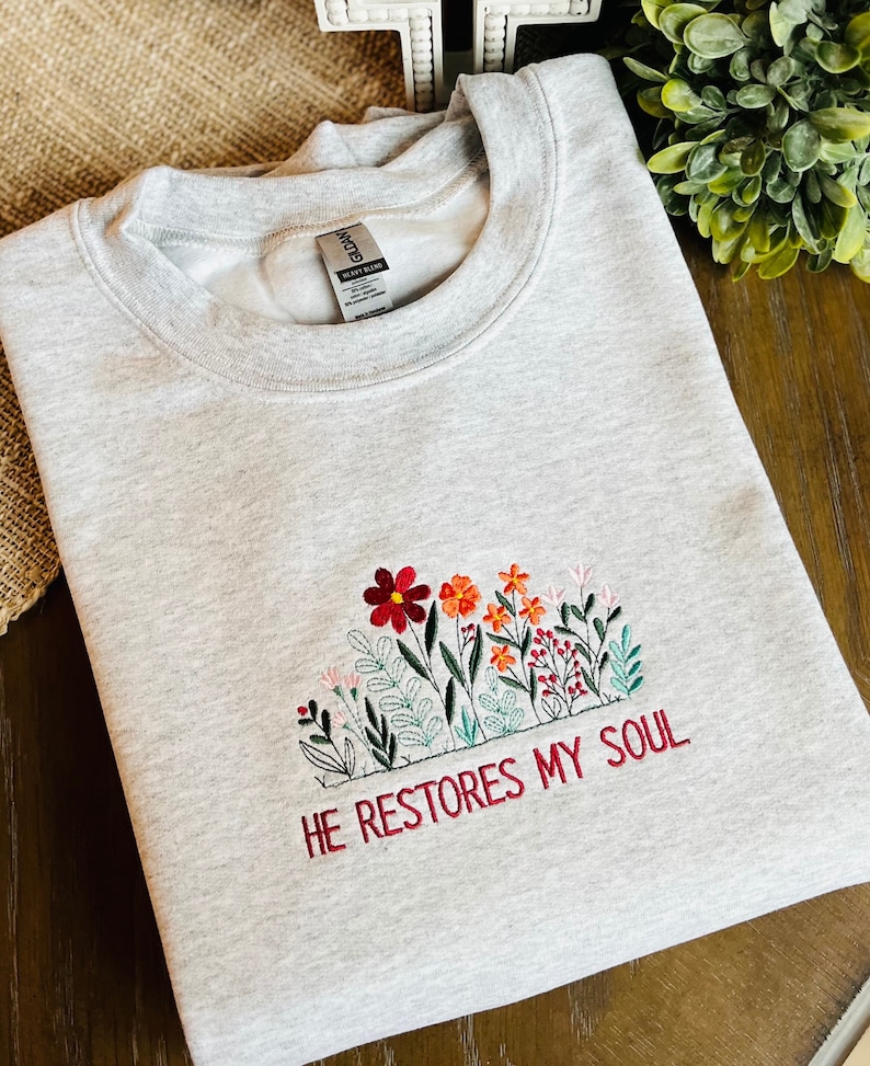 May include: Gray sweatshirt with embroidered flowers and the text "HE RESTORES MY SOUL" in red.