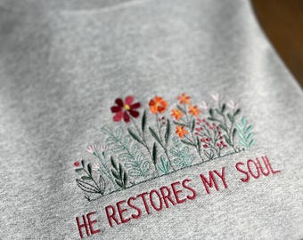 May include: Gray sweatshirt with embroidered flowers and the text "HE RESTORES MY SOUL" in red.
