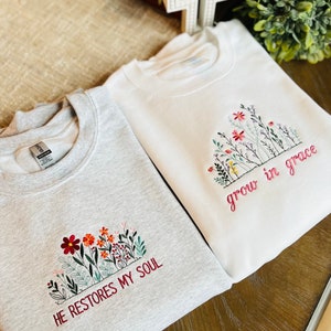 May include: Two sweatshirts with embroidered floral designs and inspirational quotes. The gray sweatshirt says "He restores my soul" and the white sweatshirt says "grow in grace".