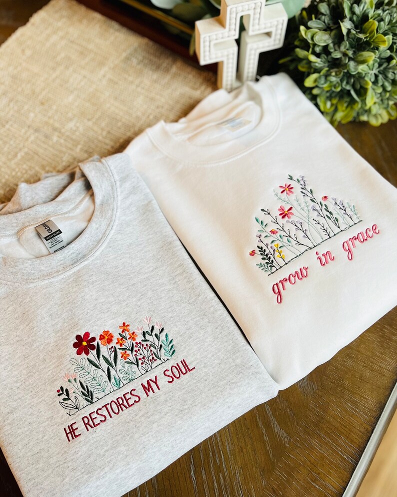 May include: Two sweatshirts with embroidered floral designs and inspirational quotes. The gray sweatshirt says "He restores my soul" and the white sweatshirt says "grow in grace".