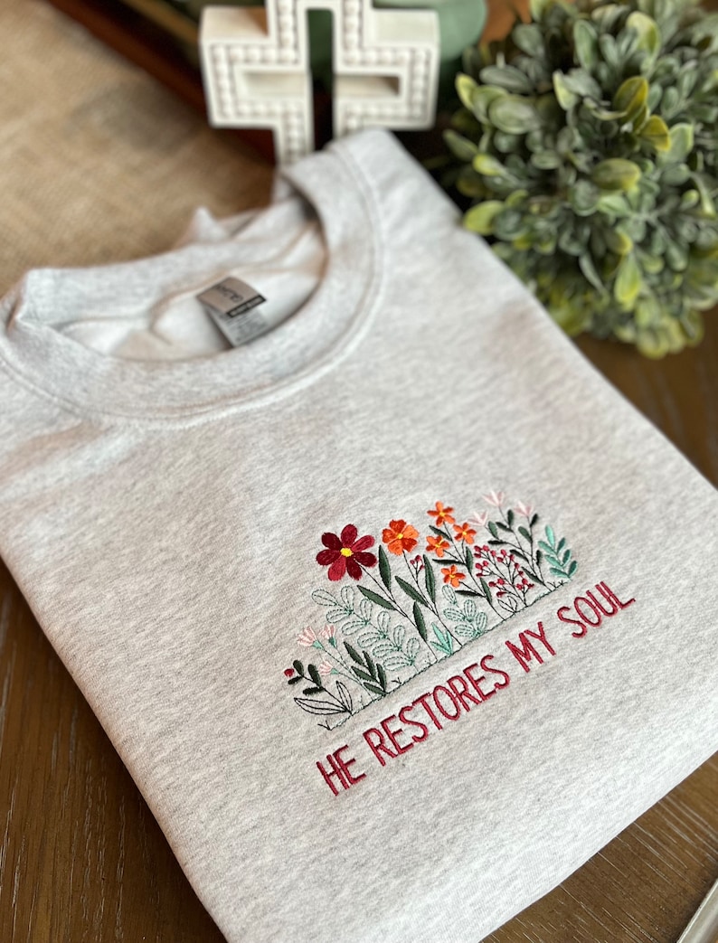 May include: Gray sweatshirt with embroidered flowers and the text "HE RESTORES MY SOUL".