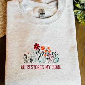 May include: Gray sweatshirt with embroidered flowers and the text "HE RESTORES MY SOUL".
