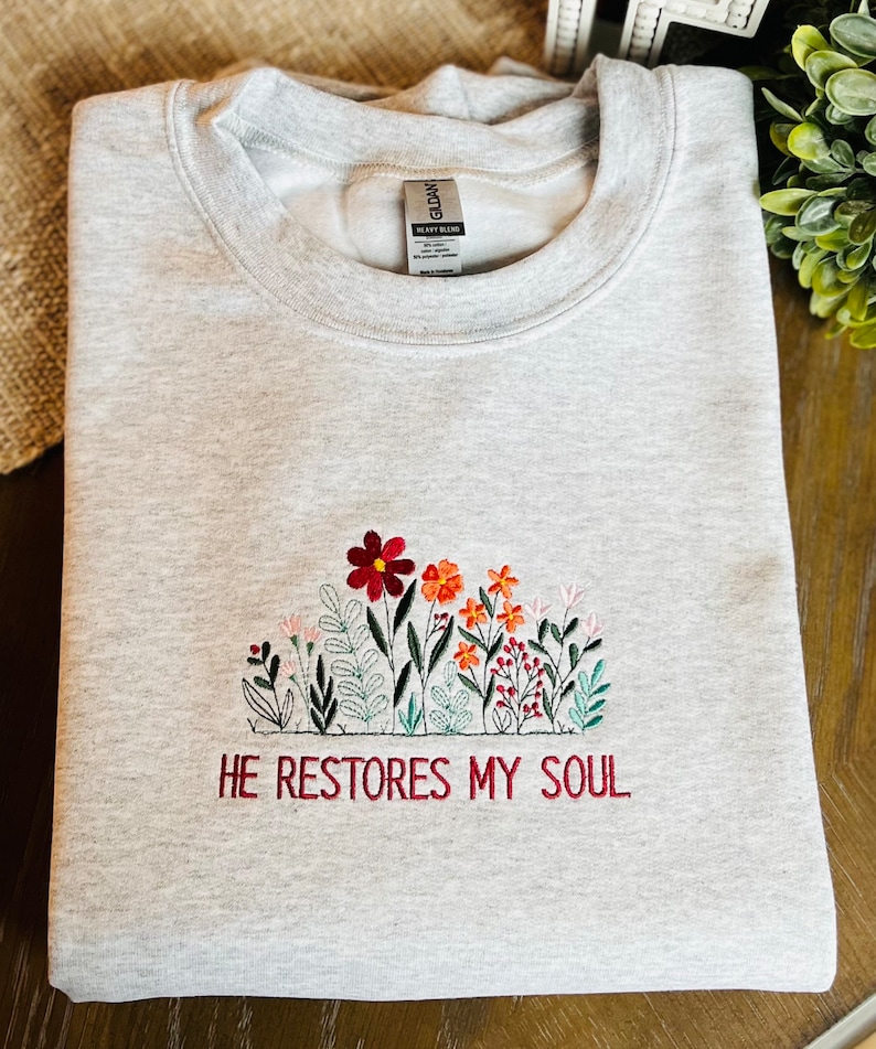 May include: Gray sweatshirt with embroidered flowers and the text "HE RESTORES MY SOUL".
