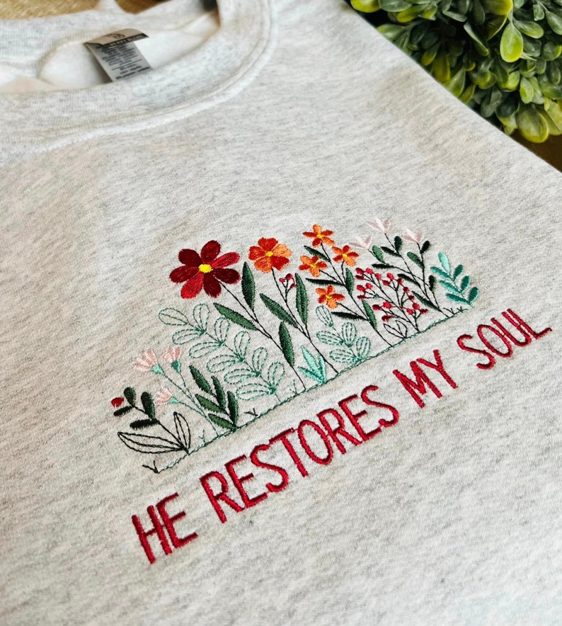 May include: Gray sweatshirt with embroidered flowers and the text "HE RESTORES MY SOUL" in red.