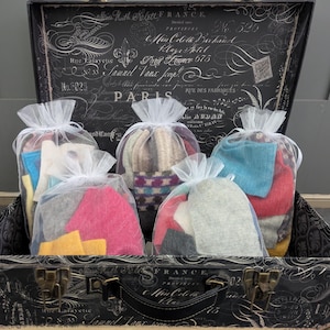 May include: Five white mesh bags filled with colorful fabric scraps. The bags are arranged in a row on top of a vintage suitcase with a black and white floral design. The suitcase has a brass latch and a handle.