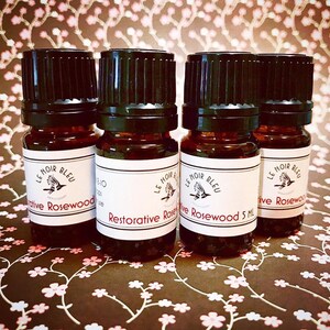 May include: Four small brown glass bottles with black caps and white labels. The labels have black text that reads "Le Noir Bleu" and "Restorative Rosewood 5 ML".