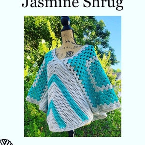 Può includere: Uno scialle all'uncinetto fatto a mano nei toni del grigio e del turchese, esposto su un manichino. Il capo presenta uno scollo a V e un motivo a zig-zag. I testi "Jasmine Shrug" e "Hello Gabby" sono visibili.