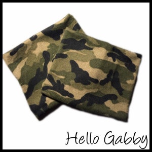 Op de afbeelding: Twee stoffen items met camouflagepatroon, waarschijnlijk nekwarmer of hoofdbanden, worden getoond. De stof heeft een mix van groene, bruine en zwarte vormen. De tekst "Hello Gabby" staat in cursief onderaan de afbeelding.