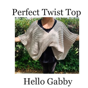 K&ouml;nnte beinhalten: Ein hellbeige, geripptes Strick-Twist-Top mit dem Text "Perfect Twist Top" und "Hello Gabby". Das Top ist &uuml;ber den Schultern und Armen drapiert. Der Hintergrund ist ein gr&uuml;ner Busch.