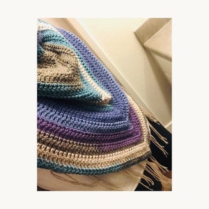 May include: A crocheted shawl with a multi-colored striped pattern in shades of blue, purple, brown, and white. The shawl has a fringe border.