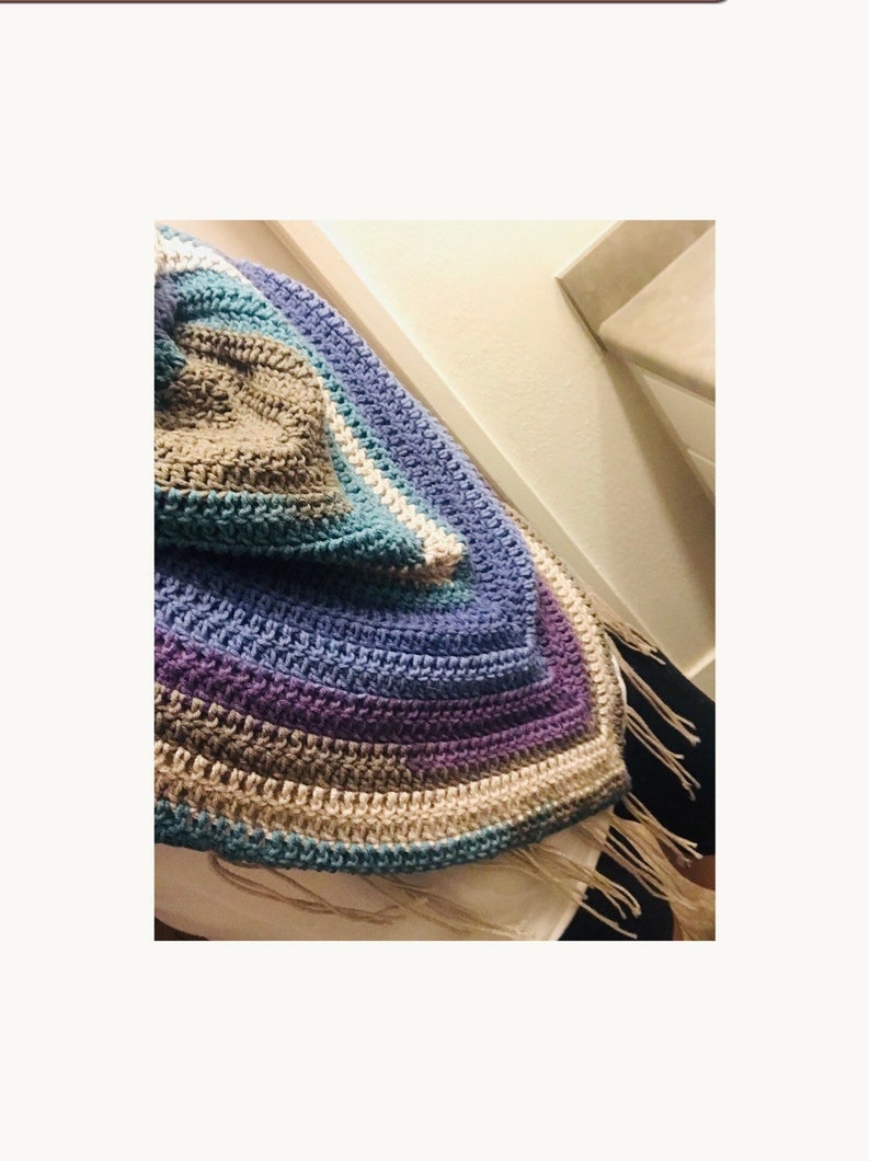May include: A crocheted shawl with a multi-colored striped pattern in shades of blue, purple, brown, and white. The shawl has a fringe border.