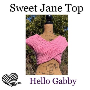 May include: A pink crocheted crop top with a V-neck and short sleeves. The top is on a mannequin and has a criss-cross design in the front. The text "Sweet Jane Top" is at the top of the image and "Hello Gabby" is at the bottom.