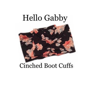 Puede incluir: Puños de bota fruncidos negros con un estampado floral en tonos rosa y crema. El texto "Hello Gabby" y "Cinched Boot Cuffs" se muestran en fuente negra.