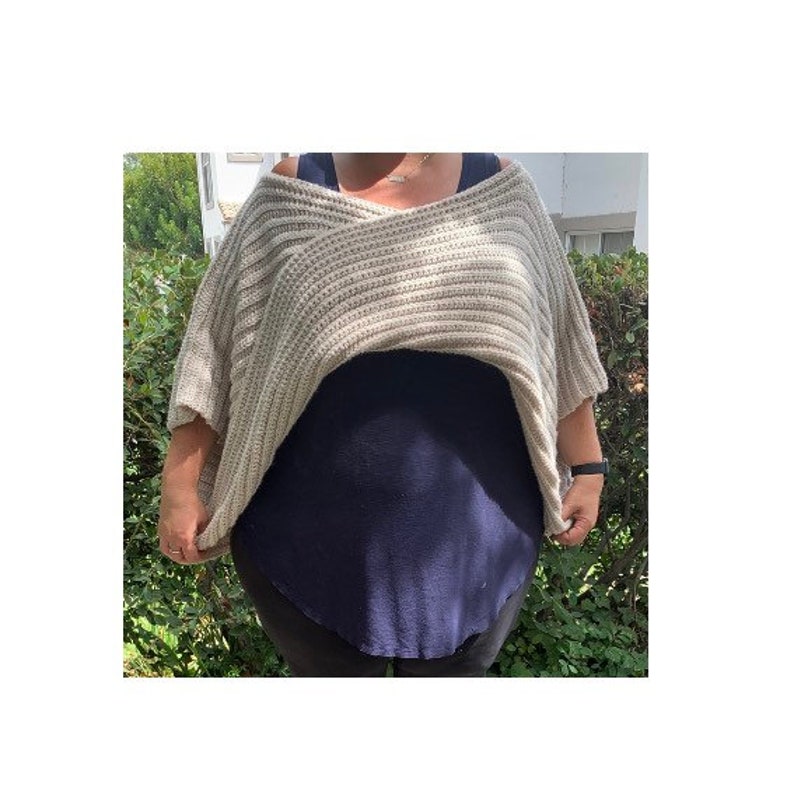 K&ouml;nnte beinhalten: Ein beigefarbener, &uuml;bergro&szlig;er Strickpullover mit V-Ausschnitt. Der Pullover hat eine gerippte Textur und kurze &Auml;rmel. Er wird &uuml;ber einem dunkelblauen Oberteil getragen. Der Stil ist l&auml;ssig und bequem.