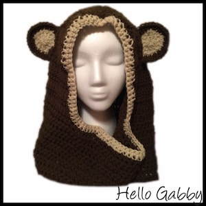 May include: Brown crocheted hooded scarf with tan ears and trim. The scarf is worn on a white mannequin head. The text "Hello Gabby" is visible at the bottom of the image.
