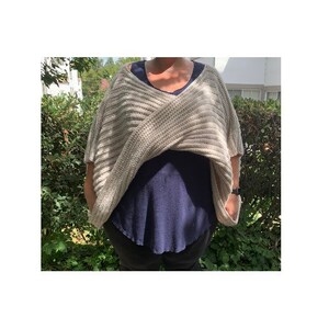 K&ouml;nnte beinhalten: Ein beigefarbener, kurz&auml;rmeliger Strick-Wickelpullover mit V-Ausschnitt. Der Wickelpullover ist &uuml;ber einem dunkelblauen Oberteil geschichtet. Der Pullover hat ein strukturiertes, horizontal geripptes Muster. Die Person tr&auml;gt eine Uhr am linken Handgelenk.