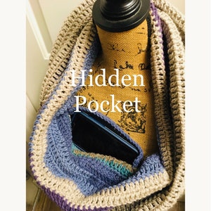 May include: A crocheted infinity scarf with a hidden pocket, shown with a cell phone inside. The scarf is made with beige, purple, and blue yarn.