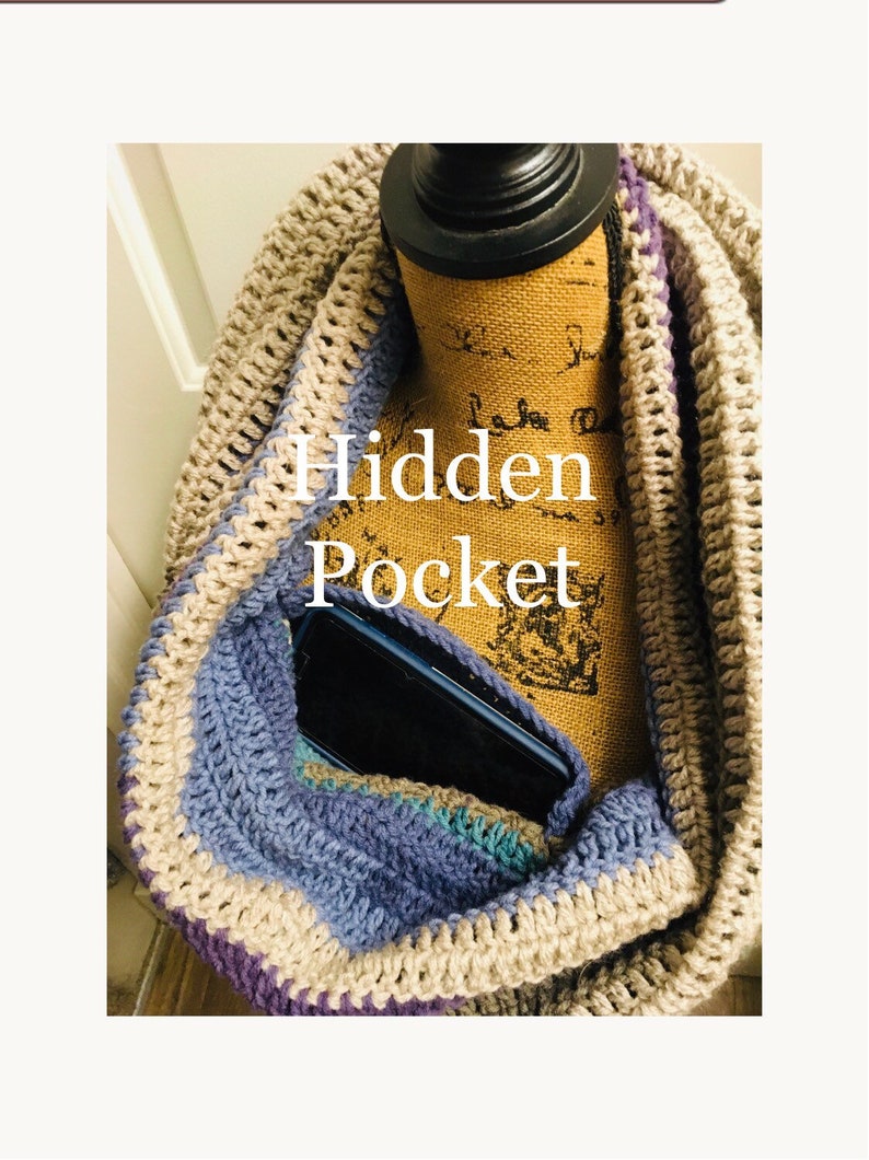 May include: A crocheted infinity scarf with a hidden pocket, shown with a cell phone inside. The scarf is made with beige, purple, and blue yarn.