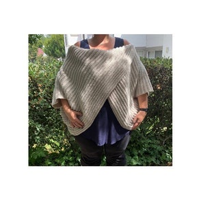 K&ouml;nnte beinhalten: Ein beiger, &uuml;bergro&szlig;er Strickwickel mit kurzen &Auml;rmeln. Der Wickel ist &uuml;ber einem dunkelblauen Oberteil und einer schwarzen Hose drapiert. Der Wickel hat eine gerippte Textur und ist aus einem weichen, neutral get&ouml;nten Garn gefertigt.