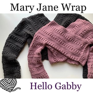 May include: Two crocheted wraps, one in dark gray and one in dusty rose, are laid out on a white surface. The wraps are both long-sleeved and have a criss-cross design. The text "Mary Jane Wrap" is at the top of the image and "Hello Gabby" is at the bottom.