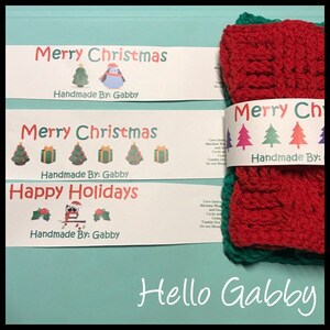 May include: A stack of red and green crocheted items with a white paper band that reads "Merry Christmas" and "Handmade By: Gabby." Additional labels say "Merry Christmas" and "Happy Holidays" with festive illustrations.