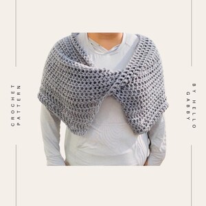 May include: A gray crochet shawl with a textured, open weave design. The shawl is draped over the shoulders. The words "CROCHET PATTERN" and "BY HELLO GABBY" are printed on the left and right sides of the image.