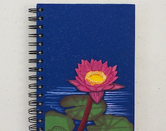 Peut inclure: Un carnet à spirales bleu avec un nénuphar rose peint sur la couverture. Le nénuphar a un centre jaune et des feuilles vertes.