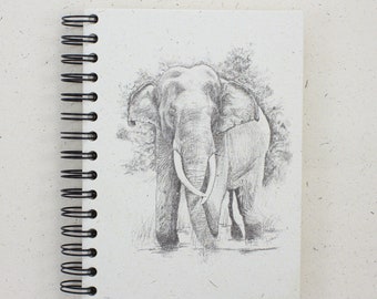 May include: A black and white pencil drawing of an elephant in a notebook. The elephant is drawn in detail, with its trunk, tusks, and ears clearly visible.