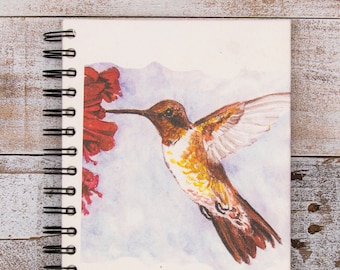 Peut inclure: Une peinture à l'aquarelle d'un colibri aux plumes brunes et jaunes, buvant du nectar d'une fleur rouge. Le colibri est en vol, les ailes déployées. L'arrière-plan est une douce aquarelle bleue et violette.