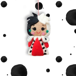 May include: A felt ornament of Cruella de Vil from Disney's 101 Dalmatians. She has black and white hair, a red dress with black spots, and a mischievous smile.